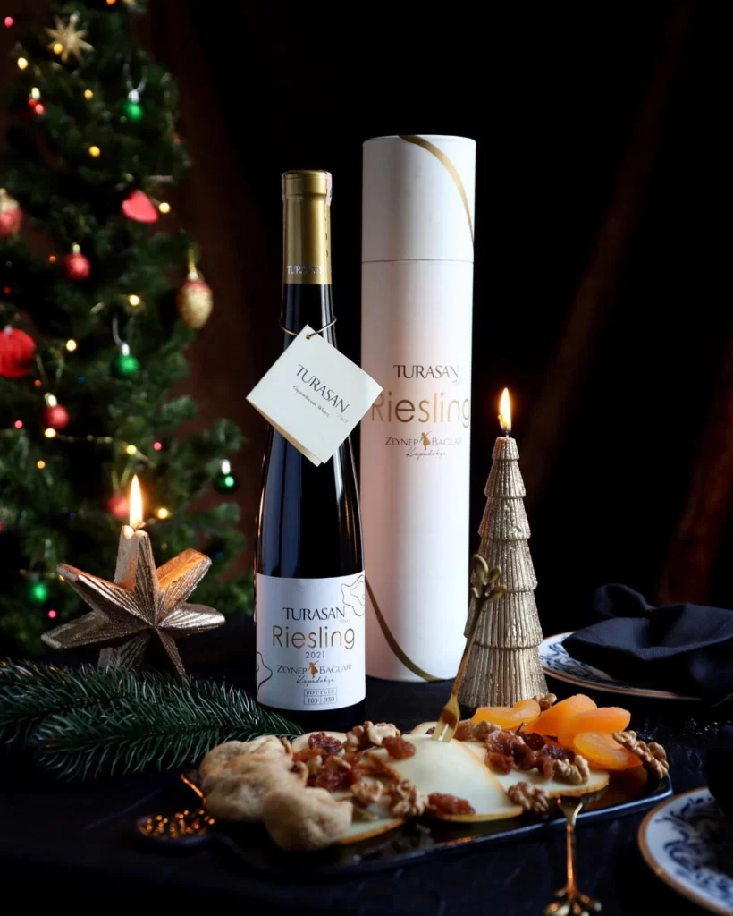 Turasan Riesling şarabı, Zeynep Bağları etiketiyle şık bir sunumda; yanında kuru kayısı, ceviz ve peynir tabağıyla yeni yıl konseptli bir masa dekorasyonu