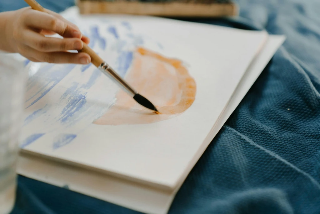 Bir çocuğun sanat terapisi sırasında fırçayla pastel tonlarda su bazlı boya çalışması yapması.