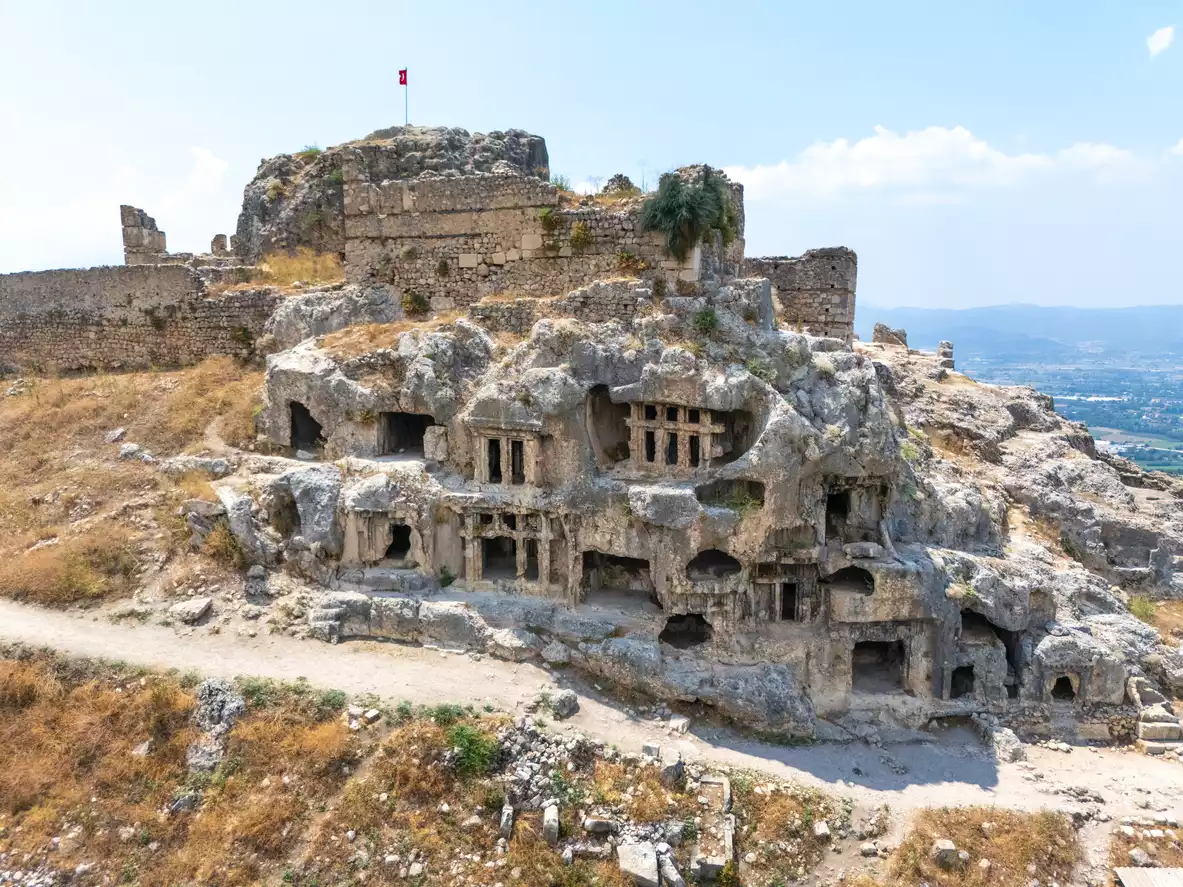 Likya antik kenti Xanthos'un geniş bir vadiye bakan tepesindeki etkileyici kaya mezarları ve sur kalıntıları, en üst noktada dalgalanan Türk bayrağı ile güneşli bir günde tarihi ve kültürel zenginliğini vurguluyor.