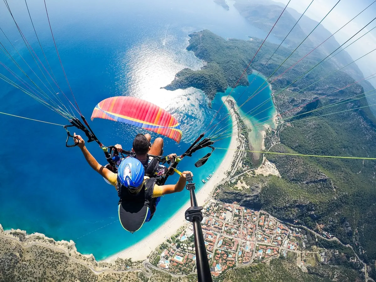 Fethiye'nin en özel tatil yerleri arasında gösterilen Ölüdeniz üzerinde yamaç paraşütü yapan iki kişi, masmavi deniz ve yeşil kıyı manzarasıyla görülüyor.