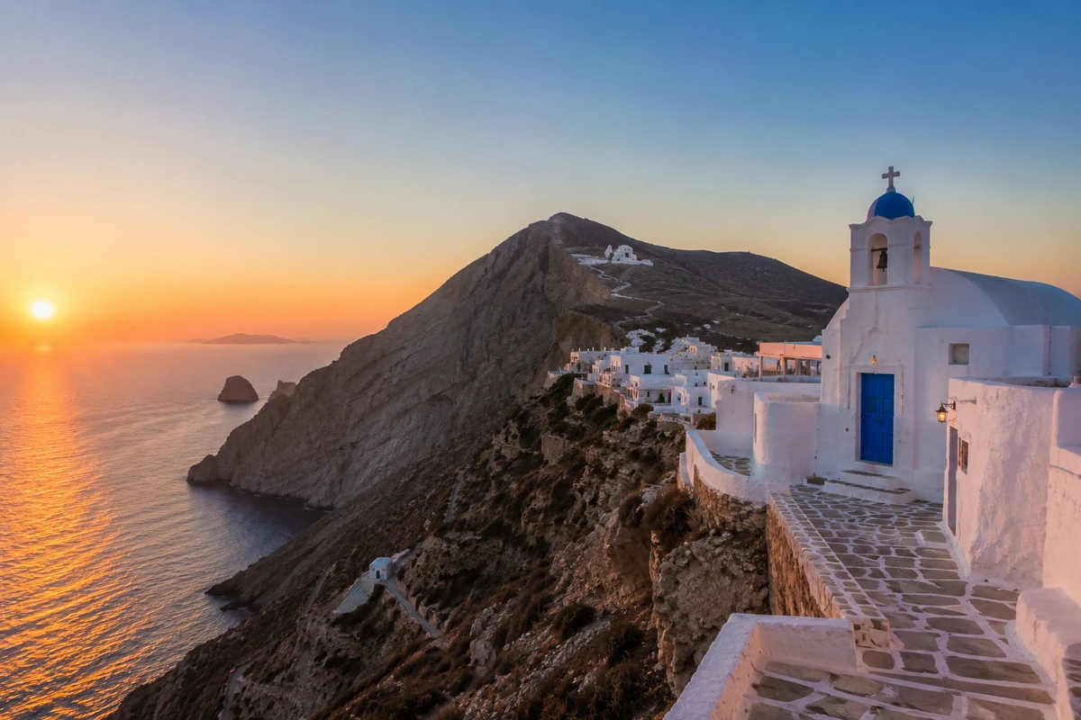 Folegandros Adası'nın sarp yamacında, gün batımının turuncu ve pembe tonlarıyla aydınlanan, denize nazır beyaz badanalı evler ve mavi kubbeli çan kulesi olan geleneksel bir kiliseyi gösteren muhteşem bir manzara, Santorini alternatifi bir güzellik sunuyor.
