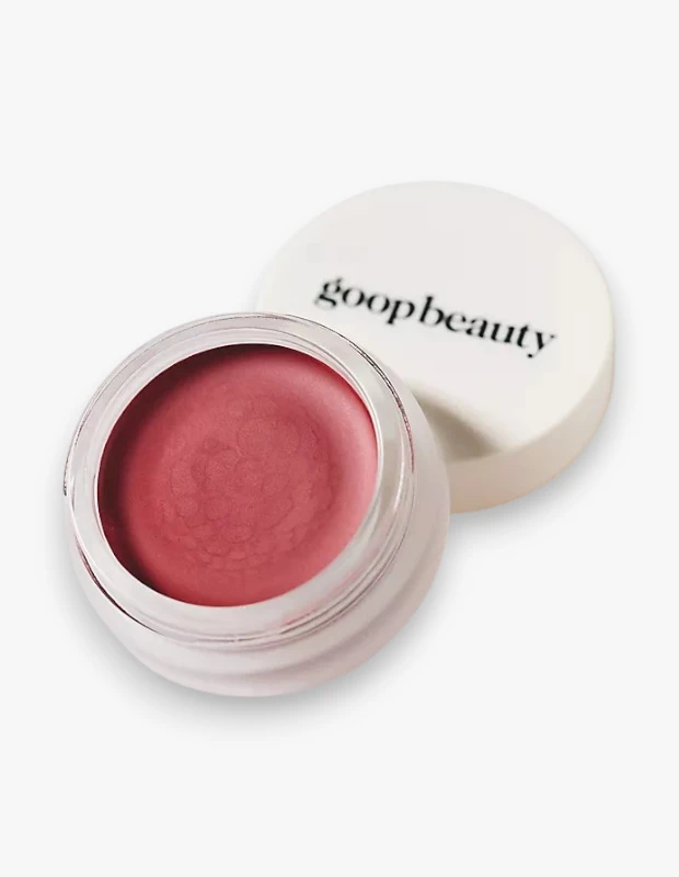 Goop Beauty markalı, parlaklık veren bir balm olan ve şeffaf cam kavanozunda duran, kapağı yanında açık halde pembe tonlu Afterglow rengi Colorblur Glow Balm ürünü, pürüzsüz ve nemli görünümüyle dikkat çekiyor.