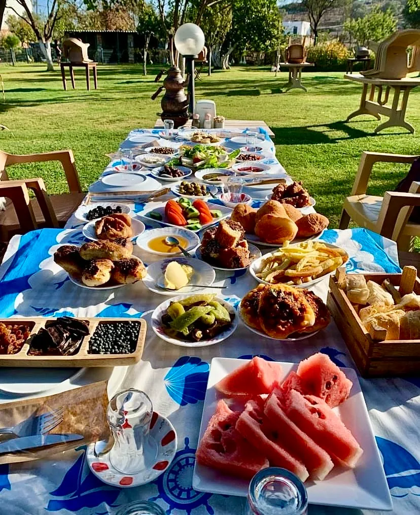 Geniş ve bakımlı yeşil bir çim alanda, mavi beyaz desenli bir örtüyle bezenmiş uzun bir masanın üzerinde, karpuz dilimlerinden zeytine, peynirden böreğe, patates kızartmasından çay bardaklarına kadar birçok lezzetin sunulduğu, güneşli bir günde kurulan zengin bir kır sofrası keyifli bir başlangıç vadediyor.