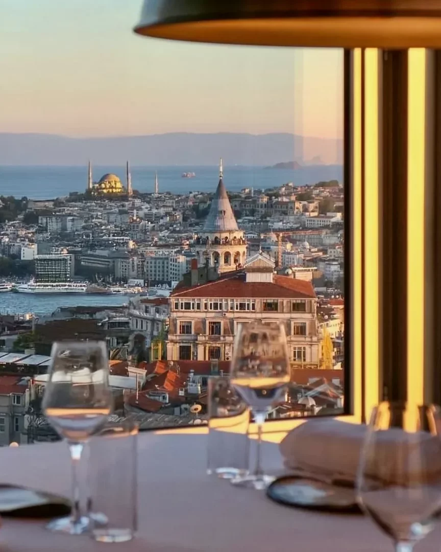 İstanbul silüetine bakan lüks restoran masasında kadehler ve gün batımı manzarası, Babalar Günü tatil önerileri içinde lezzet ve lüksü birleştiren bir rota fikri sunuyor.