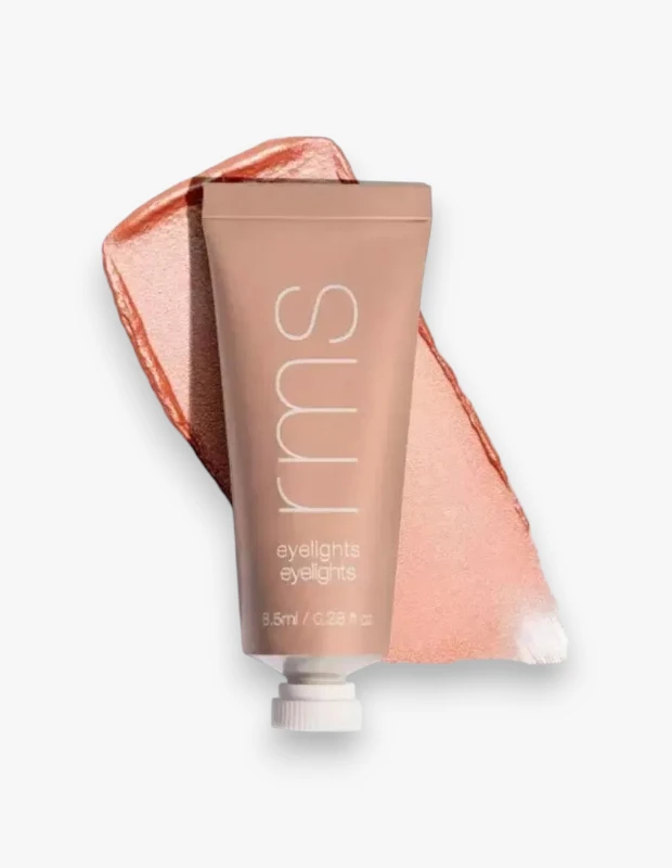 Açık bej rengindeki RMS Beauty Eyelights Krem tüpü, gözler için pürüzsüz ve kremsi dokusunu ön plana çıkaran, beyaz bir arka plan üzerinde, ışıltılı şeftali-altın tonlarında canlı bir Sunbeam renk örneğiyle birlikte göz alıcı bir şekilde duruyor.