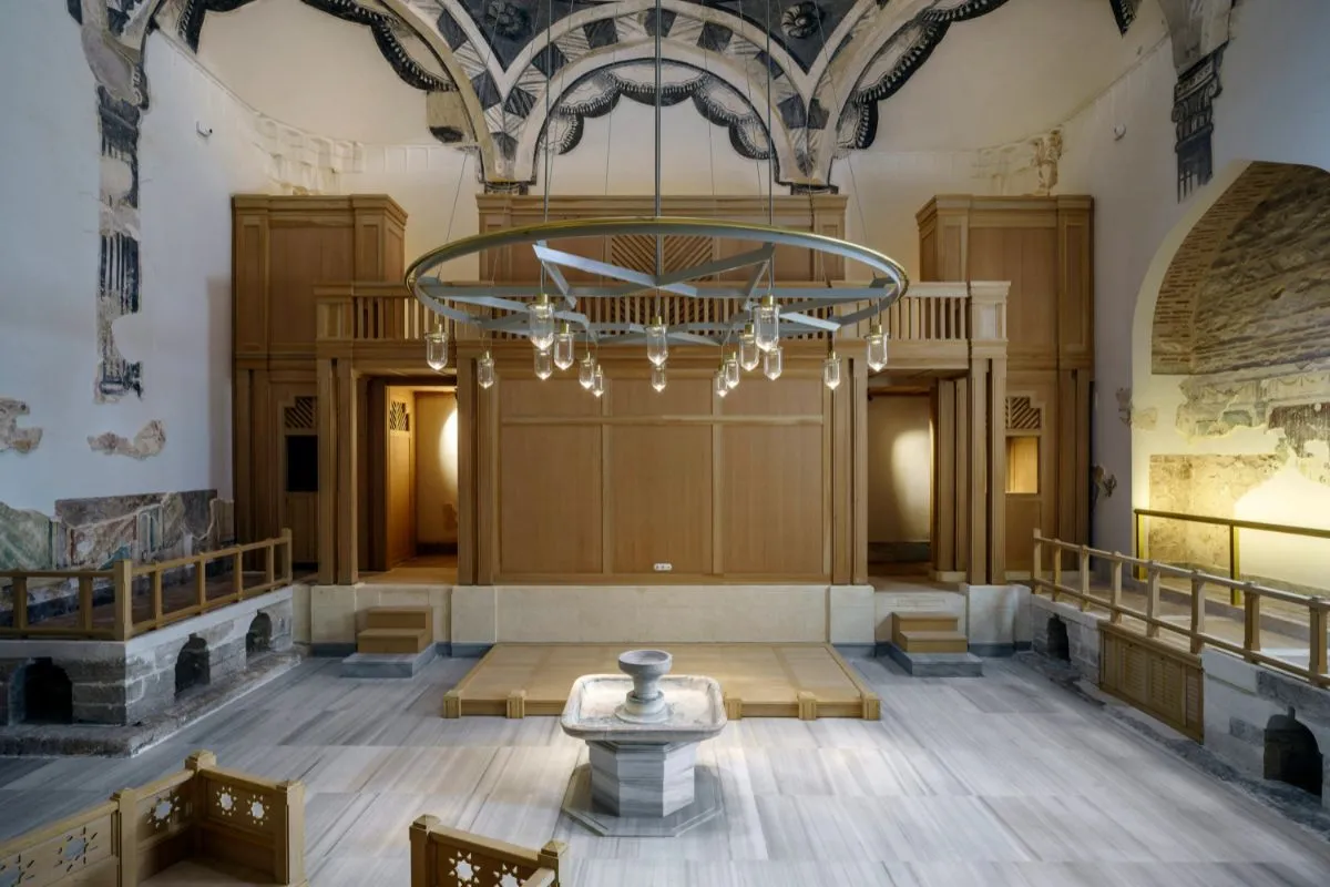 Tarihi hamam mimarisine sahip restorasyonlu iç mekân; mermer zemin, ahşap galeriler, merkezi göbek taşı ve modern aydınlatma detayları.