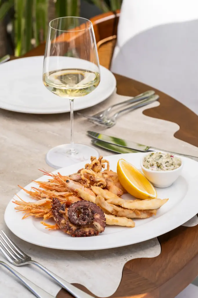 Bodrum'un en iyi restoranlarından birinde sunulan, iştah açıcı kızarmış karides, çıtır kalamar ve ahtapot parçalarından oluşan bol kepçe bir karışık deniz ürünleri tabağı, yanında tazeleyici limon dilimi, kremalı yeşil sos ve zarif bir kadeh beyaz şarap ile şık bir masada servis edilmiş.