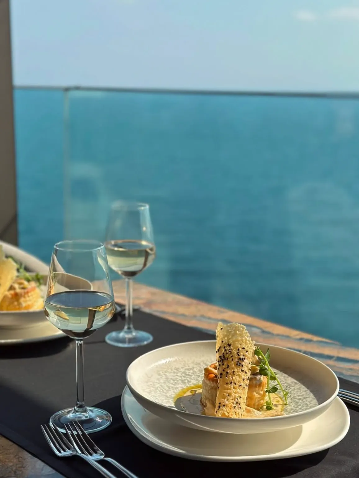 Lanthe Restaurant'ta masada, denizin açık mavi sularının manzarası eşliğinde, güneşin yansıdığı iki kadeh beyaz şarap ve özenle hazırlanmış gurme yemekler, keyifli bir yemek deneyimini gözler önüne seriyor.