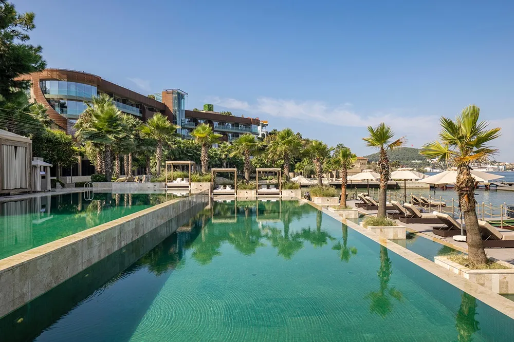Büyükada'daki Princes' Palace Resort'un, modern mimarisi ve yemyeşil palmiye ağaçları arasında konumlanmış, denize nazır turkuaz renkli geniş sonsuzluk havuzu ile lüks güneşlenme alanlarını gözler önüne seren nefes kesici bir manzara.