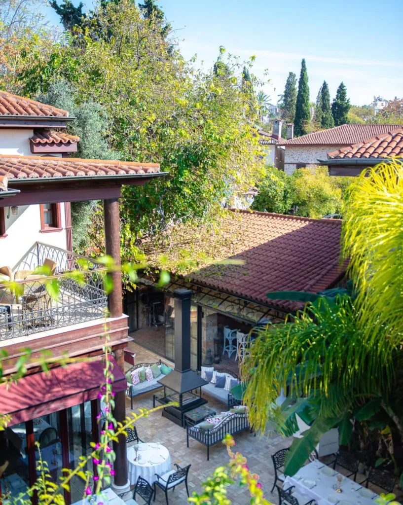 Tuvana Otel'in geleneksel kiremit çatılı binalar arasında konumlanmış, yemyeşil bitkilerle çevrili, açık hava yemek masaları ve konforlu oturma gruplarının bulunduğu avlusu, dinlendirici ve huzurlu bir atmosfer sunuyor.