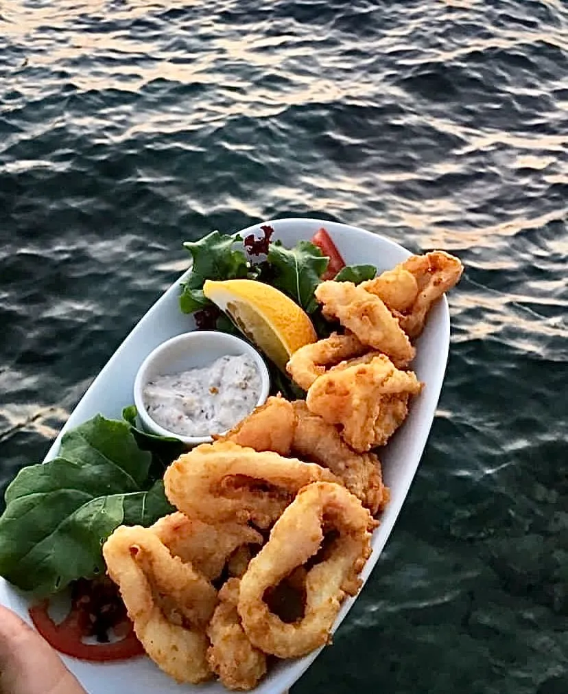 Marmaris'teki Ahtapotçu Mehmet Usta'nın muhtemelen spesiyali olan, yanında limon dilimi, yeşillik ve sosla servis edilmiş, dışı çıtır çıtır içi yumuşacık bol porsiyon kalamar tava ve benzeri deniz ürünleri, dalgalı denizin romantik gün batımı ışıklarıyla parlayan yüzeyinin önünde iştah açıcı bir şekilde sunuluyor.