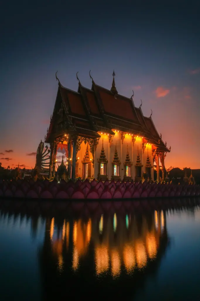 Tayland’ın Bangkok şehrinde gün batımında ışıklarla aydınlanan Budist tapınağı ve suya yansıyan silueti.