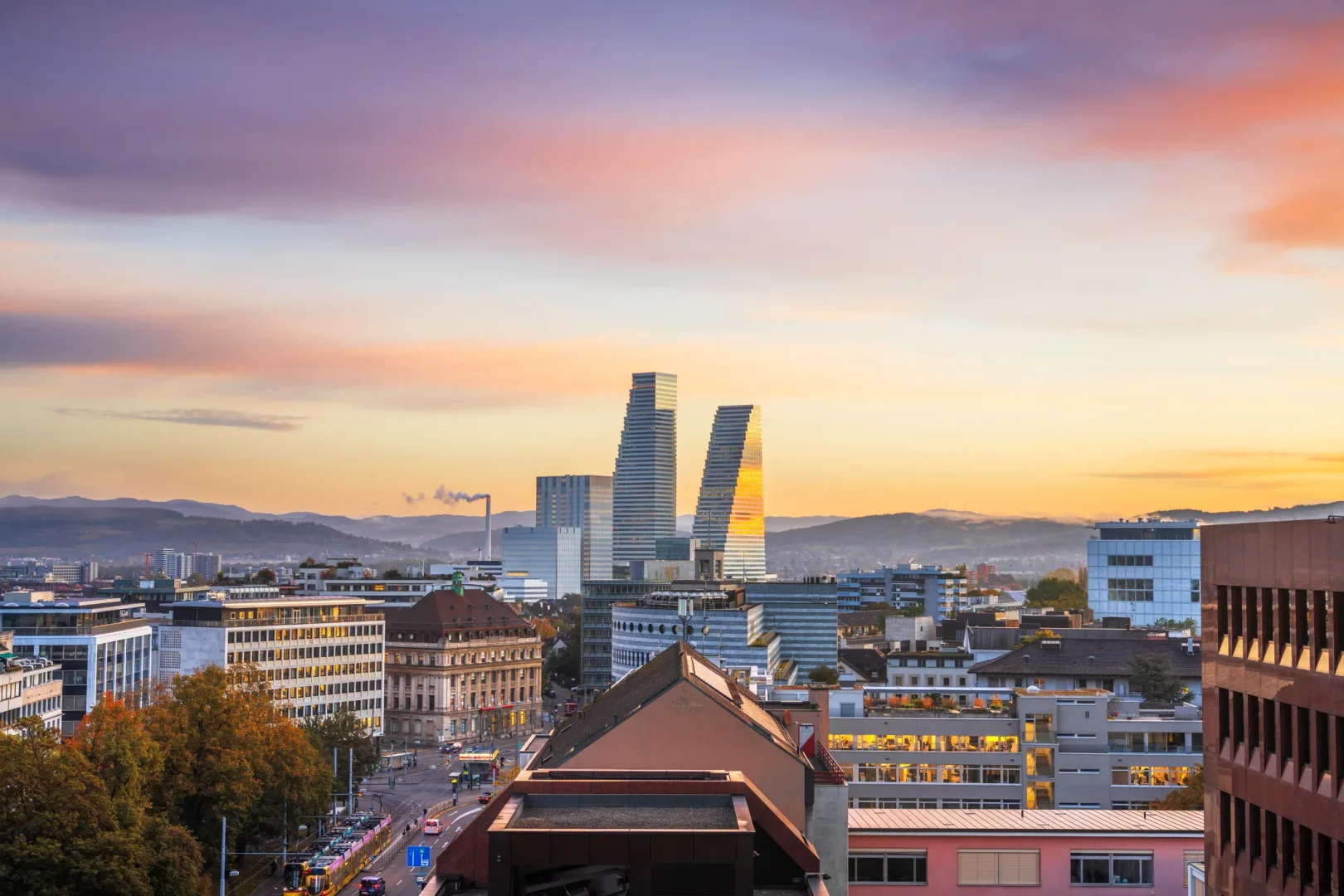 Basel gezilecek yerler arasında modern silüetiyle öne çıkan Roche Kuleleri ve gün batımında çağdaş şehir manzarası.