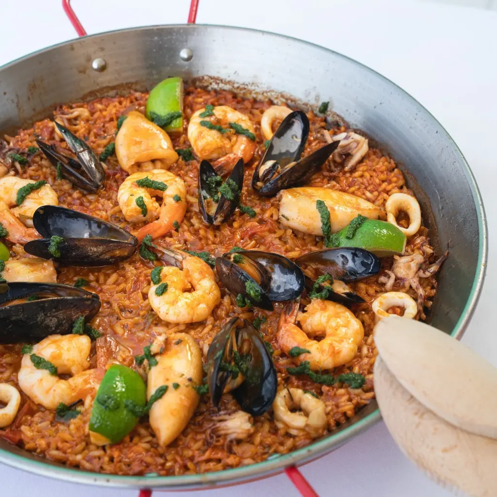 Canlı renkli, iri karidesler, taze midyeler ve yumuşak kalamar halkalarıyla zenginleştirilmiş, misket limonu ve yeşil ot sosuyla süslenmiş bu paella, Bodrum'un en iyi restoranları arasında yer alan ve çeşitli lezzetler sunan mekanların ruhunu yansıtıyor.