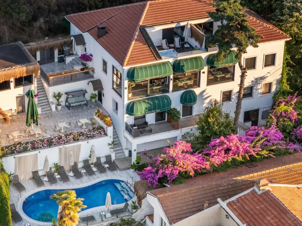Büyükada’da, havuzlu terası ve rengarenk begonvillerle çevrili lüks bir butik otel, yaz akşamı ışığında üstten görüntülenmiş.