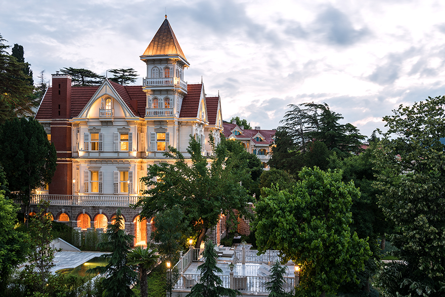 Büyükada’da tarihi mimarisi ve ışıklandırmasıyla dikkat çeken zarif bir otel, yemyeşil ağaçlar arasında gün batımı ışığında parlıyor.