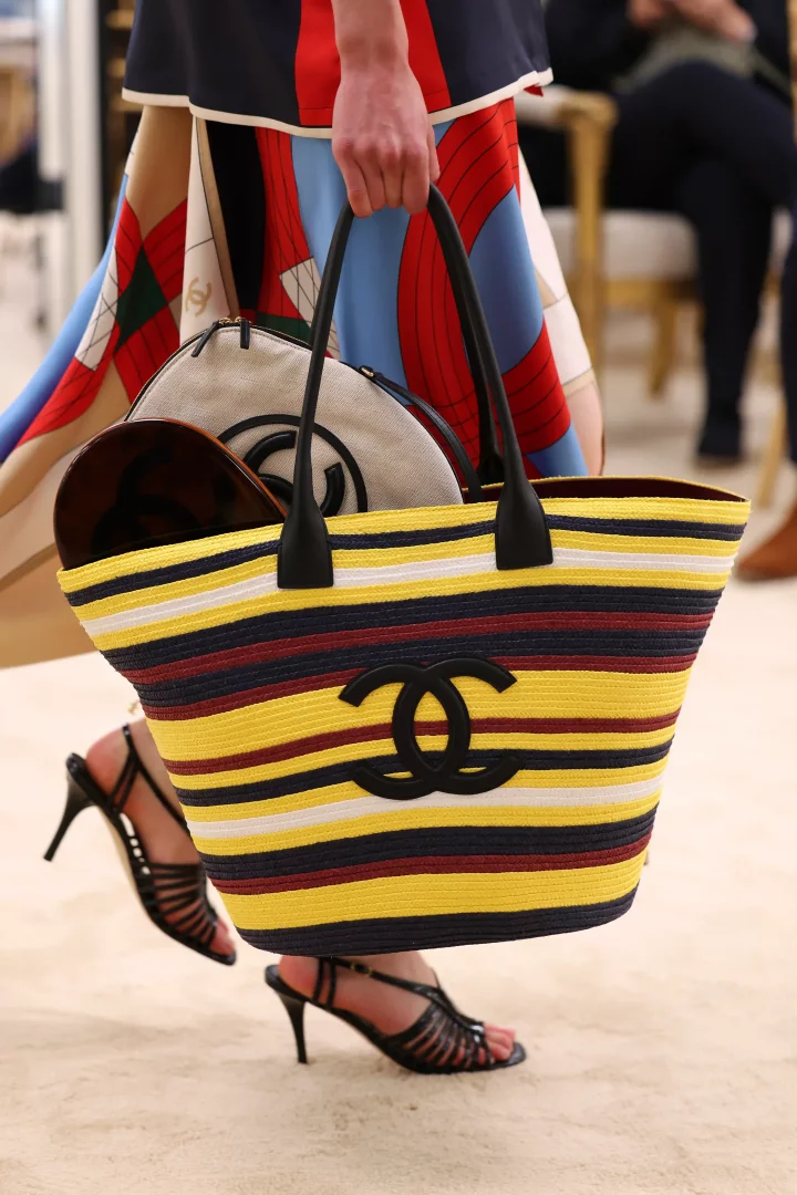 Canlı sarı, koyu mavi, bordo ve beyaz yatay şeritleriyle dikkat çeken, siyah deri saplı büyük bir Chanel hasır çanta taşıyan model, içinde markanın logolu başka bir çantayla birlikte yaz gardırobunun vazgeçilmezi olan hasır çantaların modern ve lüks yorumunu sergiliyor.
