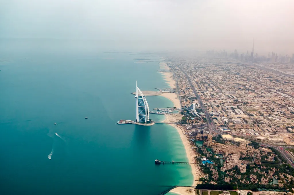 Dubai sahil şeridinde, denizin üzerine inşa edilmiş Burj Al Arab ve şehir silüetinin yer aldığı havadan bir görüntü.