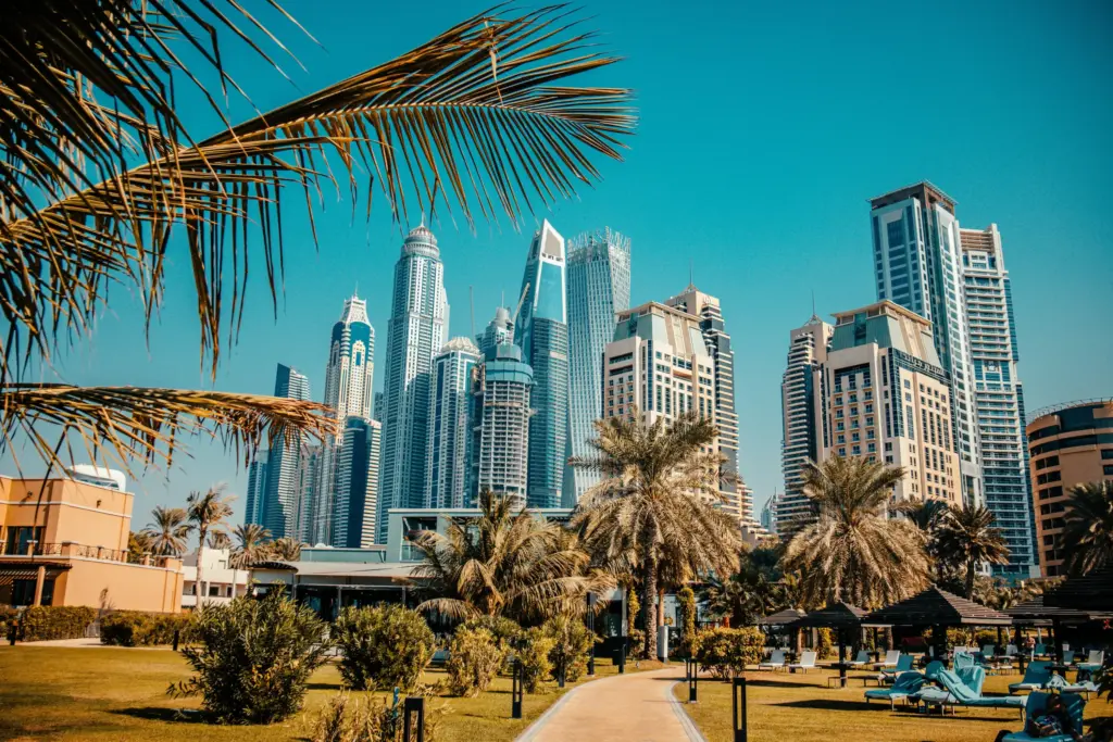 Dubai Marina bölgesinde modern gökdelenler, palmiye ağaçları ve lüks otel bahçeleriyle şehir manzarası.