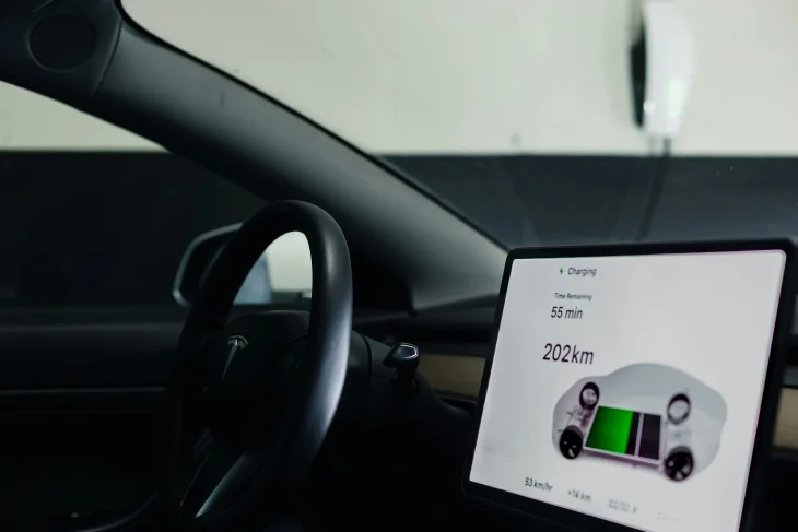 Bir elektrikli otomobilin içinden çekilmiş bu görselde, direksiyon simidinin yanında yer alan büyük dokunmatik ekranda 55 dakika şarj süresi kaldığı ve mevcut şarjla 202 km menzil gidilebileceği bilgisi, batarya durumunu gösteren grafiksel bir araç çizimiyle birlikte net bir şekilde okunuyor.