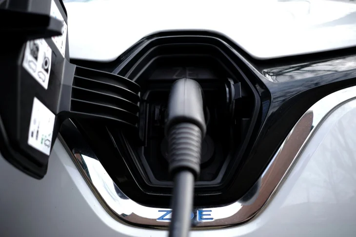 Beyaz bir elektrikli otomobilin ön kısmında yer alan şarj portuna takılı koyu gri şarj kablosu, araç markası ZOE yazısıyla birlikte elektrikli otomobillerde menzil artırma ve şarj etme süreçlerinin temelini açıkça gösteriyor.