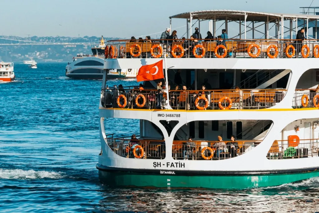 İstanbul Boğazı’nda yolcu taşıyan Şehir Hatları vapuru, güvertesinde yolcular ve dalgalanan Türk bayrağıyla mavi sularda ilerliyor.