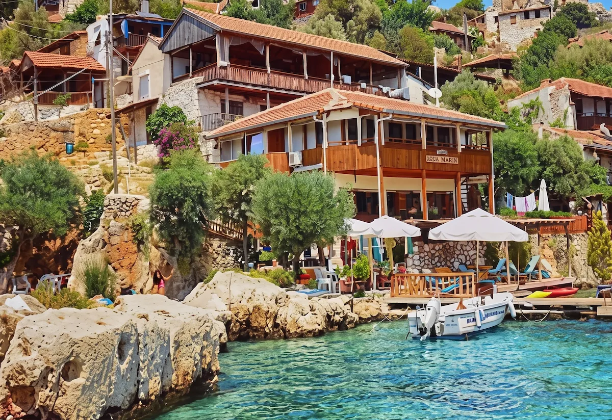 Gökçeada'nın Kaleköy sahilinde, turkuaz berraklığındaki denizin kıyısında, yamaçlara serpişmiş taş ve ahşap mimarili otantik evlerin ve Aqua Marin adlı tesisin bulunduğu, güneşli bir günde teknelerin demirli olduğu iskeleyle şezlongların denize nazır uzandığı, yemyeşil ağaçlarla çevrili sakin bir Deniz manzarası.