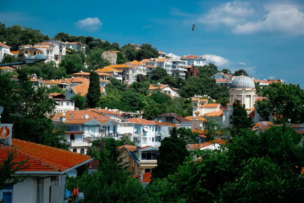 Kınalıada’nın yamaçlarındaki beyaz ve turuncu çatılı evler, arka planda Aya Todori Kilisesi’nin kubbesi ve masmavi gökyüzü.