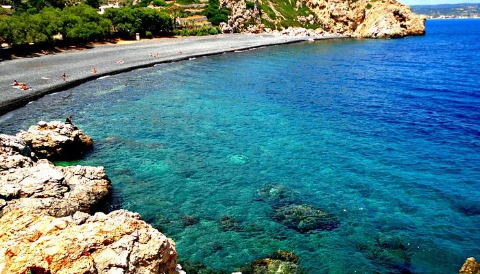 Sol tarafta koyu renk çakıl taşlarından oluşan bir sahile sahip, berrak turkuaz ve lacivert sularıyla dikkat çeken, kayalıklarla çevrili Mavra Volia plajı, güneşlenen ve yüzen birkaç kişiyle huzurlu bir manzara sunuyor.