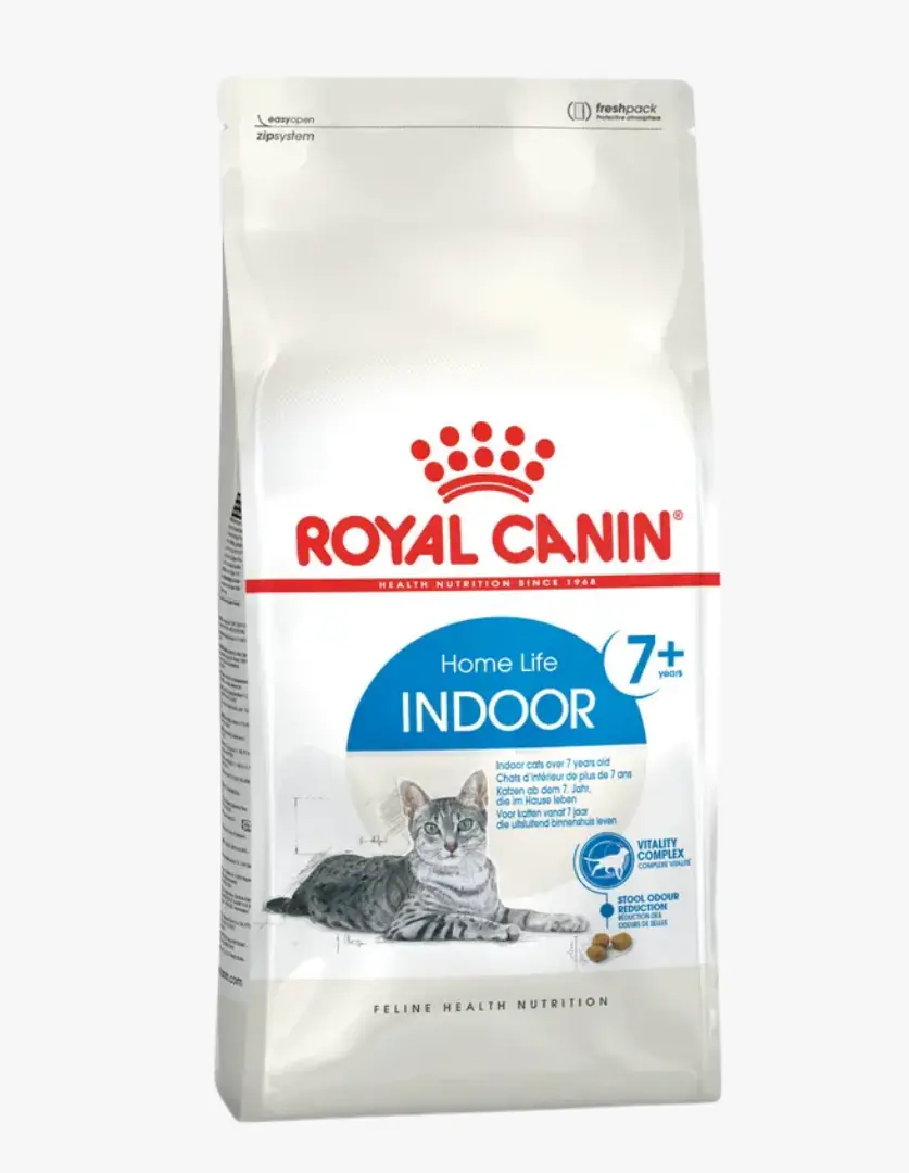 Beyaz ambalajında, gri renkli bir tekir kedi resminin ve markanın kırmızı logosunun yer aldığı, özellikle 7 yaş üzeri ev kedileri için tasarlanmış Royal Canin Indoor 7+ kedi maması paketi, birkaç mama tanesiyle birlikte net bir şekilde sergileniyor.