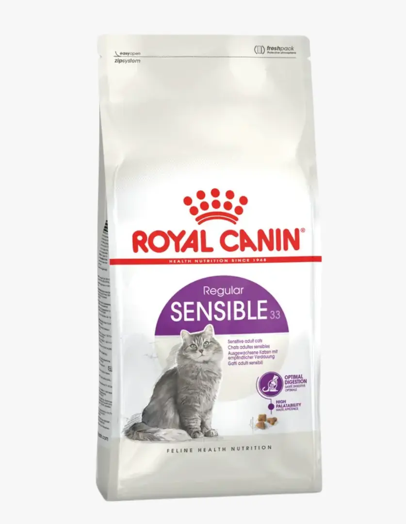 Beyaz bir zeminde dik duran, Royal Canin logosu ve Sensible 33 ibaresi belirgin şekilde görülen, üzerinde gri tüylü bir kedi ve birkaç mama tanesi resmi bulunan, hassas sindirime sahip yetişkin kediler için özel olarak üretilmiş Royal Canin Sensible 33 kedi maması paketidir.