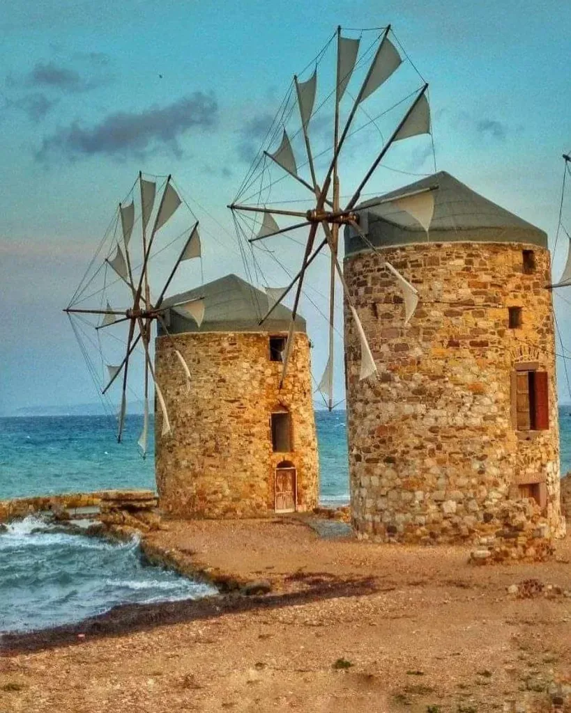 Sakız Adası'nın sahilinde yükselen, yelkenleri olan iki tarihi taş yel değirmeni, masmavi Ege Denizi'nin dalgalarıyla yıkanan kıyının romantik atmosferini vurgularken, bu eşsiz gezilecek yerlerden birini gözler önüne seriyor.
