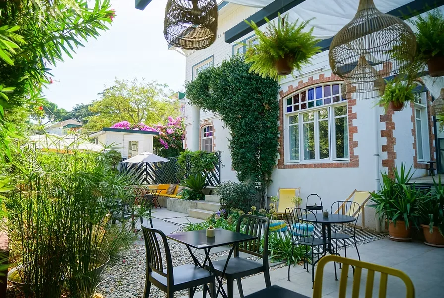 Büyükada’daki Sergüzeşt Otel’in yemyeşil bahçesi, modern masa ve sandalyelerle düzenlenmiş huzurlu bir açık hava alanı.
