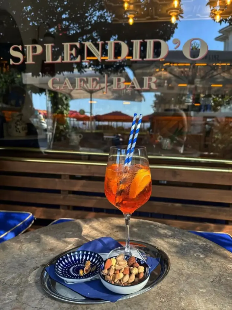 Splendid’O Cafe Bar’ın önünde, mermer masada servis edilmiş Aperol Spritz ve yanında kavrulmuş kuruyemişler.
