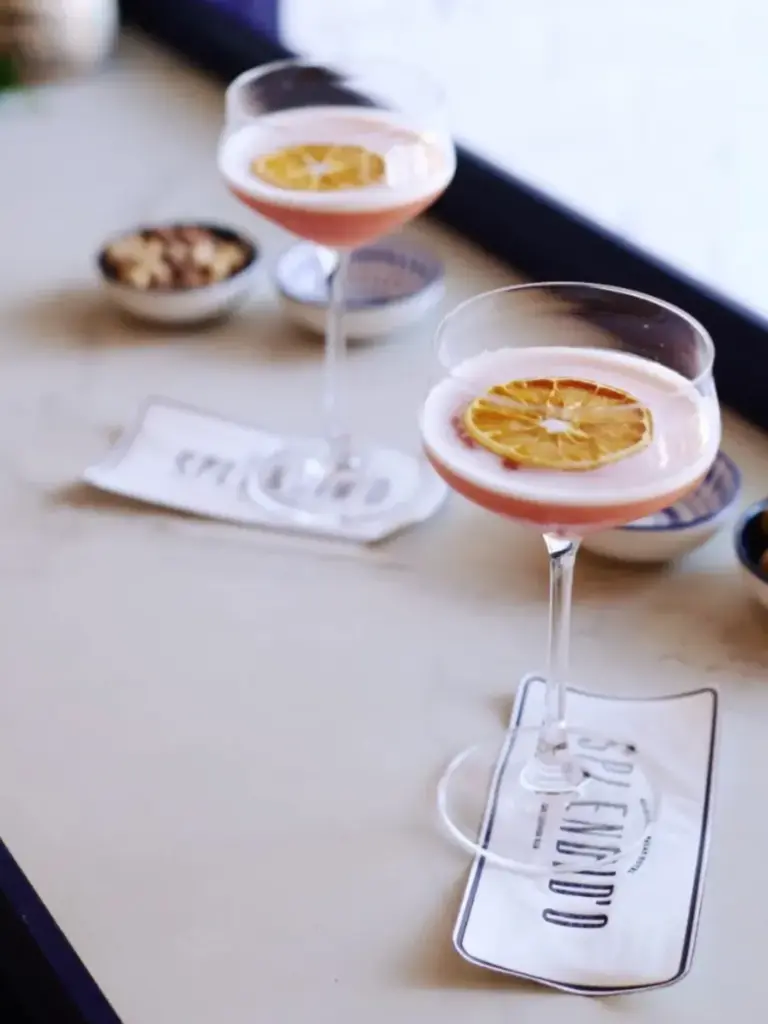 Splendid’O Cafe Bar’da servis edilen, kurutulmuş portakal dilimiyle süslenmiş pembe kokteyller ve yanında küçük atıştırmalık kaseleri.