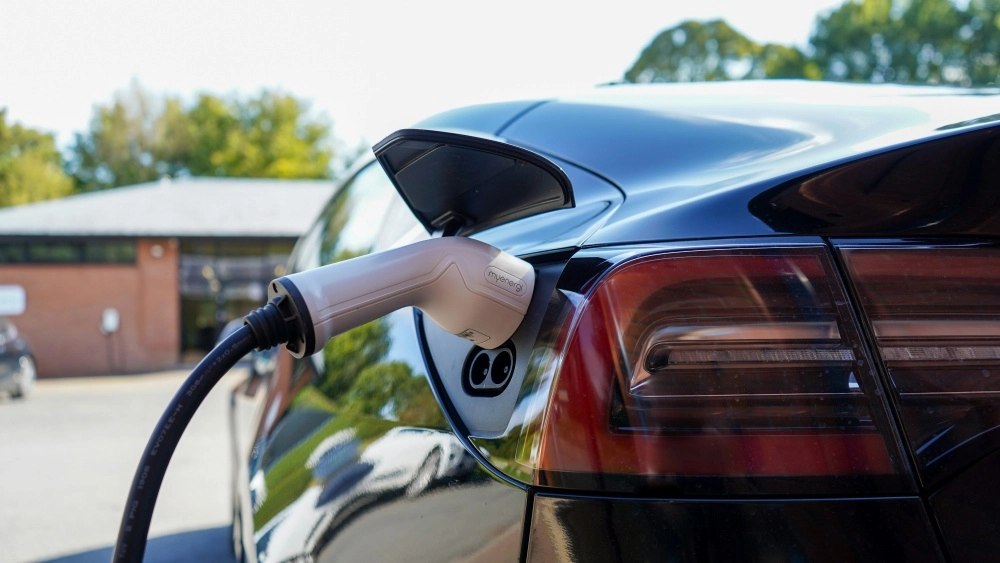 Siyah renkteki bir Tesla Model Y elektrikli otomobil, açık şarj portuna takılı myenergi markalı gri şarj kablosuyla dışarıda bataryasını doldururken görülüyor, bu durum elektrikli araçların menzilini ve şarj imkanlarını vurguluyor.