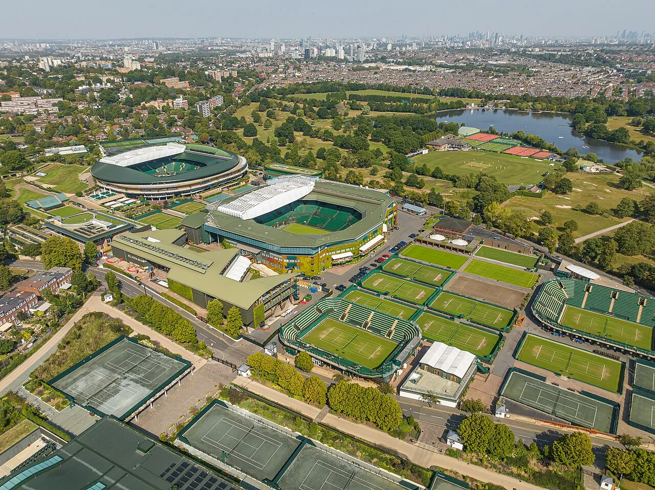 Londra'daki Wimbledon tenis kompleksinin kuşbakışı görünümü, şampiyonaya ev sahipliği yapan geniş yeşil çim kortları, büyük stadyumları ve çevresindeki ağaçlık alanlar ile şehrin silüetini gözler önüne seriyor.
