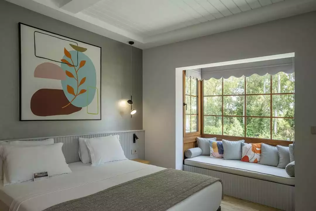 Akyaka'nın doğayla iç içe zarafetini yansıtan Balèze Boutique Hotel'deki bu modern tasarımlı, konforlu oda; beyaz nevresimli yatağı, soyut duvar sanatı ve yemyeşil ağaçlara nazır, ahşap çerçeveli büyük penceresinin önündeki minderli, şık oturma alanıyla Gökova Körfezi'nin sakin nefesine uygun dingin bir atmosfer sunuyor.