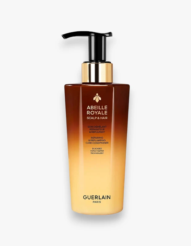 Guerlain Abeille Royale saç bakımı serisinden, siyah pompalı ve parlak altın renkli boyunlu, üst kısmı koyu kahverengiden dibe doğru kademeli olarak açık sarıya dönüşen, etiketinde onarıcı ve dolgunlaştırıcı bakım kremi yazan, arı sembollü şık bir şişe beyaz zeminde konumlanmış.