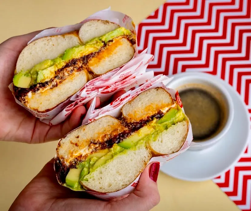 House of B'de servis edilen, ikiye bölünmüş ve avokado, peynir ve özel soslu bir bagel sandviç'in yakın çekim fotoğrafı.