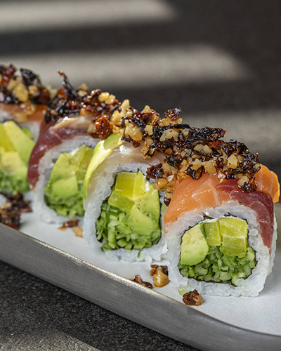Ken Sushi & More'da masada servis edilen, üzerinde somon füme, avokado ve kurutulmuş domates bulunan, farklı soslarla zenginleştirilmiş özel bir sushi tabağı