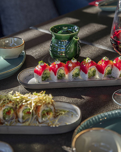 Ken Sushi & More restoranında masada servis edilmiş, üzerinde bol miktarda avokado ve özel sos bulunan, farklı çeşitlerde hazırlanmış sushi ruloları ve yanında sosluk görünüyor.
