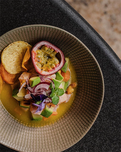 Suadiye'deki Machi'de servis edilen, bir kasede avokado, kırmızı soğan, balık ve passiflora meyvesi ile süslenmiş bir ceviche tabağının yakın çekimi. Yanında tortilla cipsleri de duruyor.