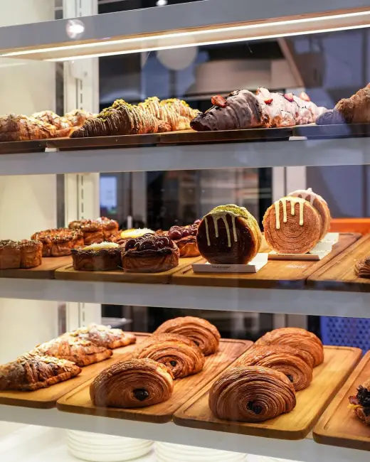 Caddebostan'da bulunan Sour & Sweet Artisan Bakery'nin vitrininde farklı çeşitlerdeki taze kruvasan ve çöreklerin sergilendiği bir bölüm. Vitrinde çikolatalı, bademli, Antep fıstıklı ve çeşitli dolgulu ürünler ahşap sunum tabaklarında düzgünce dizilmiş halde görünüyor.