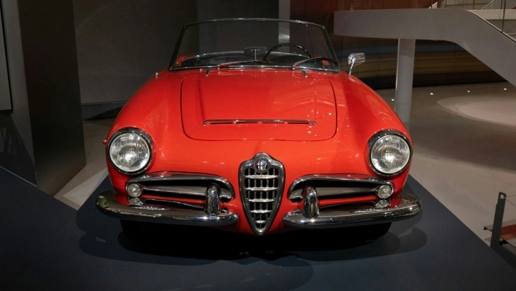 Kırmızı Alfa Romeo Spider Duetto, müzede sergilenen ön cephe görünümüyle. İtalyan otomobil tasarımının zarif çizgilerini yansıtan klasik roadster model.