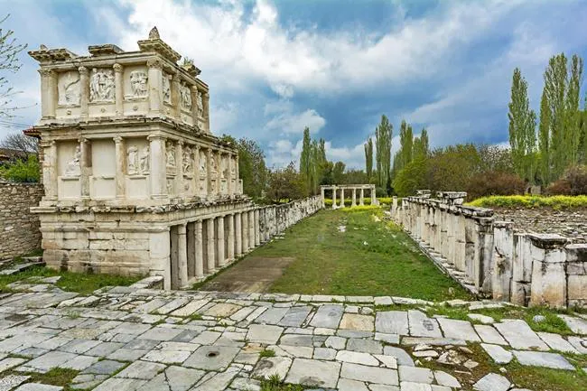 Aphrodisias Antik Kenti’ndeki heykeltıraşlık okulunun zenginliğini yansıtan, üzerinde detaylı mermer kabartmaların ve sütunların bulunduğu Sebasteion yapısı ile geniş Agora alanı, Türkiye’nin önemli UNESCO Dünya Mirası alanlarından biri olarak yemyeşil ağaçların arasında görünüyor.