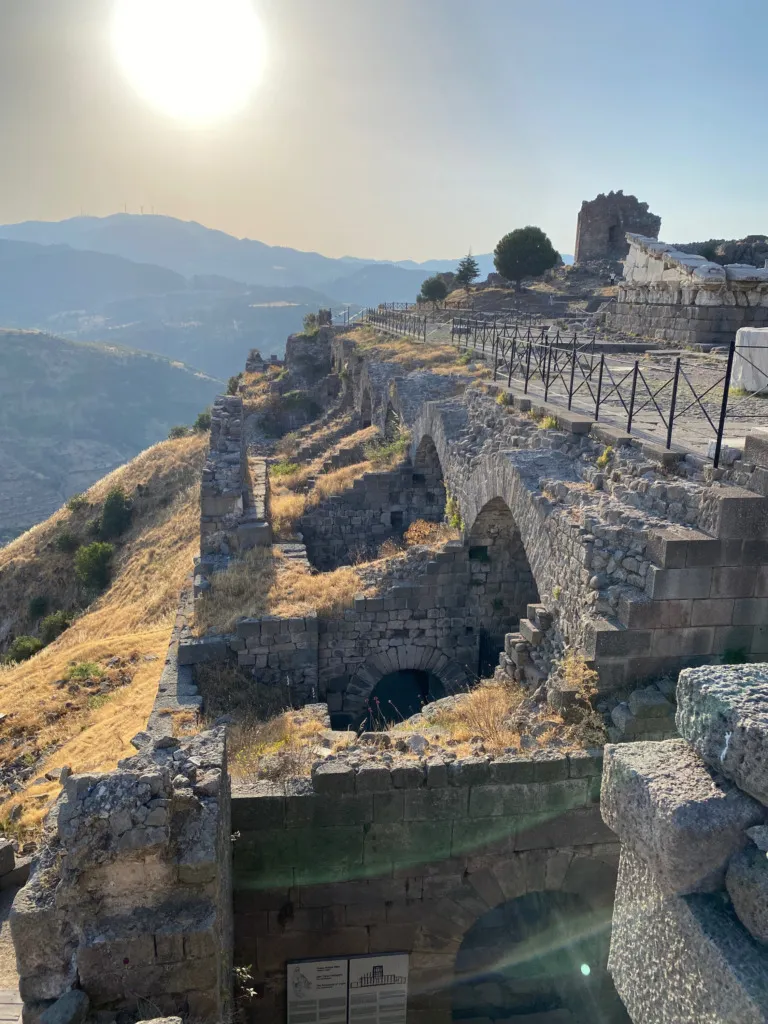 Bergama Akropolü'nde, güneşli bir günde, dağlık araziye oyulmuş katmanlı antik sur ve teras kalıntıları, Türkiye'nin UNESCO Dünya Mirası listesindeki zengin kültürel peyzajlardan birini gözler önüne seriyor.