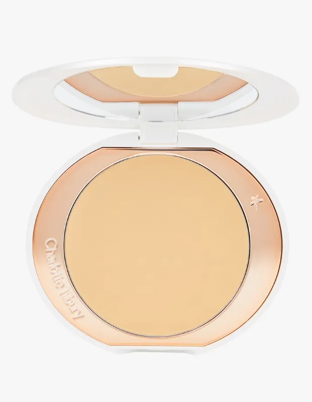 Beyaz kasalı, içi rose gold detaylı ve açık bej renkte kompakt pudra, kapağında ayna yansımalarıyla açık duruyor; Charlotte Tilbury'nin aydınlatıcı ve kusursuz bitiş sağlayan ürününü yakından gösteriyor.