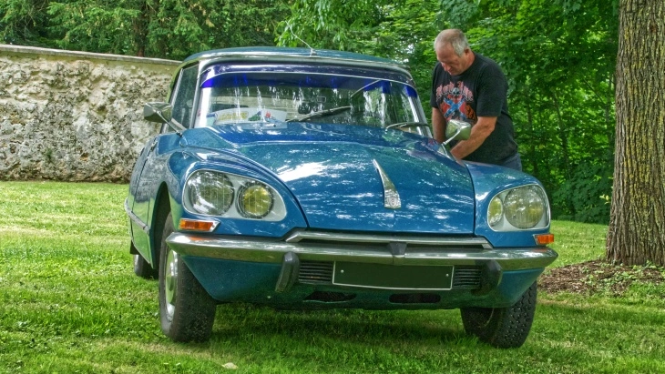 Mavi renkli klasik Citroën DS, ağaçların arasında çim alanda sergileniyor. Fütüristik tasarımı ve karakteristik farlarıyla dikkat çeken Fransız otomobili.
