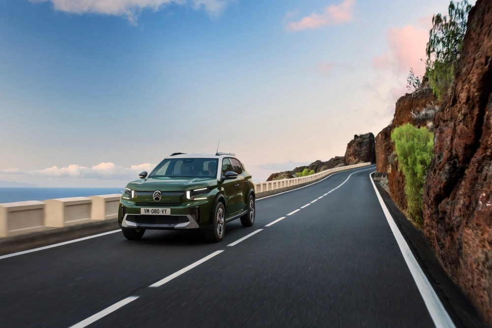Yeşil renkli Citroen e-C3 Aircross elektrikli SUV, güneşli bir günde kayalık yamaçlar ve denizin eşlik ettiği kıvrımlı sahil yolunda ilerlerken, modern dış mekan tasarımını gözler önüne seriyor.